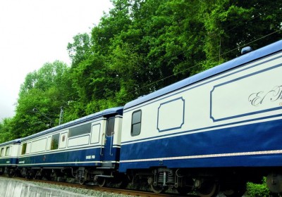 El Transcantabrico luxury train cars with blue and cream livery surrounded by lush green forest