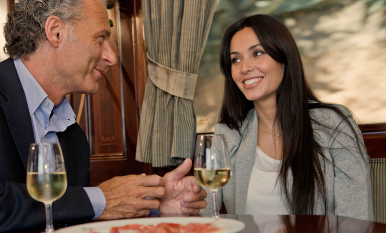 Couple enjoying wine and conversation in elegant dining car of Transcantabrico luxury train